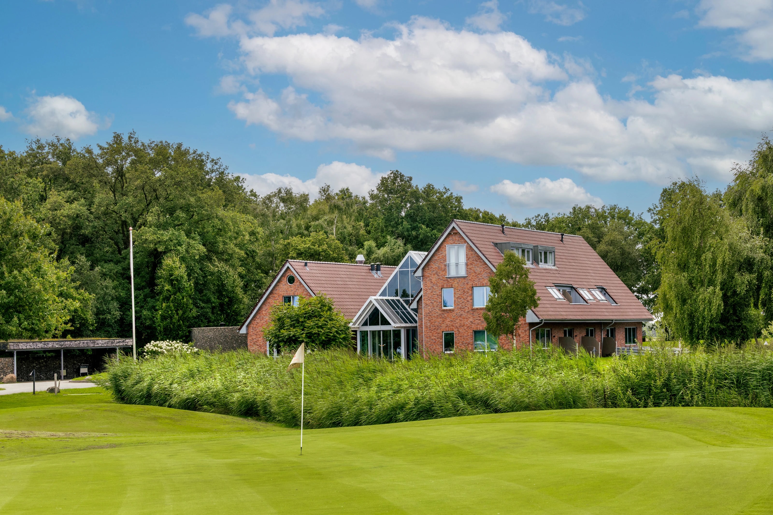 Cozmoss Boutique Hotel in het groen van Drenthe, met de glazen serre en het rode pand tussen de bomen